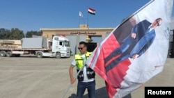 A man waves a flag with a picture of Egyptian President Abdel Fattah el-Sisi in front of the Rafah crossing, where trucks carrying humanitarian aid for Palestinians in Gaza wait for the reopening of the crossing on Oct. 17, 2023.
