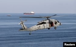 FILE - MH-60S helicopter hovers in the air with an oil tanker in the background as the USS John C. Stennis makes its way to the Gulf through the Strait of Hormuz, Dec. 21, 2018.