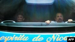 El presidente nicaragüense Daniel Ortega (D) y su esposa y vicepresidente Rosario Murillo saludan desde el interior de un autobús durante la conmemoración del 40 aniversario del retiro táctico a Masaya, el 6 de julio de 2019, en Managua. 