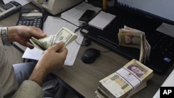 A currency exchange bureau worker counts US dollars, as Iranian bank notes are seen at right with portrait of late revolutionary founder Ayatollah Khomeini, in downtown Tehran, December 21, 2011. 