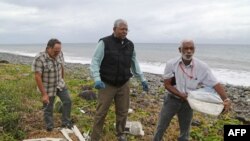 Seorang pakar Malaysia (tengah) melihat potongan-potingan pesawat di pantai di Saint-Andre de la Reunion, Pulau Reunion, Samudera Hindia (4/8). (AFP/Richard Bouhet)