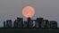 Sheep graze as the full moon, known as the "Super Pink Moon", sets behind Stonehenge stone circle near Amesbury, Britain.