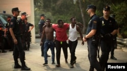 Police stand around a group of African migrants after they crossed the border fence from Morocco to Spain's North African enclave of Ceuta, Spain, Aug. 7, 2017.