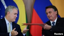 El presidente de Colombia, Iván Duque, y el presidente de Brasil, Jair Bolsonaro, intercambian documentos durante una reunión en el Palacio Planalto en Brasilia, Brasil, el 19 de octubre de 2021.