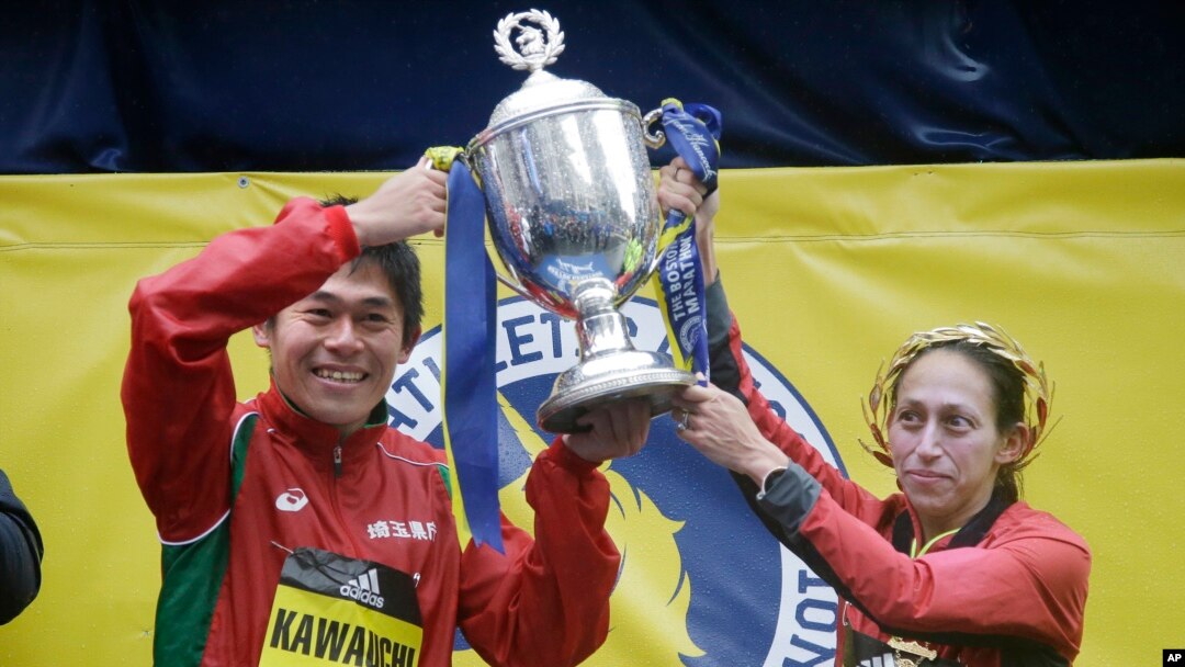 Yuki Kawauchi, kiri, dariJepang, dan Desiree Linden, dari Washington, Michigan, mengangkat trofi setelah masing-masing memenangi gelar juara untuk peserta pria dan perempuan pada Maraton Boston ke-122, 16 April 2018. 