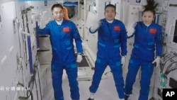 A screen grab taken at Beijing Aerospace Control Center in Beijing, China, Oct. 16, 2021, and released by Xinhua News Agency, shows three Chinese astronauts waving after they entered China's Tiangong space station core module Tianhe. 