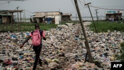 FILE: A man walks on plastic waste, used to reclaim a swamp so that the land can be developed for housing, in the Mosafejo area of Lagos, Nigeria, Feb. 12, 2019. Recently-elected President Bola Tinubu has suspended Nigeria's recent 10% tax on many plastic items. 