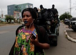 FILE - A woman walks past Cameroonian elite Rapid Intervention Battalion (BIR) members as they sit on their military vehicle during their patrol in the city of Buea in the anglophone southwest region, Cameroon, Oct. 4, 2018.