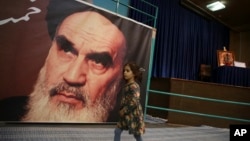 A girl walks past a poster of Ayatollah Ruhollah Khomeini, at a mosque where he made speeches, in northern Tehran, Iran, Jan. 22, 2019.