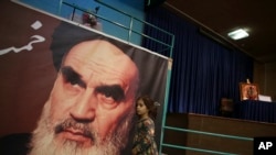 FILE - A girl walks past a poster of Ayatollah Ruhollah Khomeini, at a mosque where he made speeches, in northern Tehran, Iran, Jan. 22, 2019.