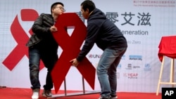 Dua pria memindahkan pita merah dalam acara untuk mendorong kesadaran akan uji HIV di Beijing, China (27/11). (AP/Ng Han Guan)