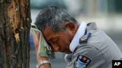 FILE - A security guard wearing an electric fan on his neck wipes his sweat on a hot day in Beijing, Monday, July 3, 2023.