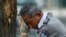 FILE - A security guard wearing an electric fan on his neck wipes his sweat on a hot day in Beijing, Monday, July 3, 2023.