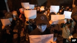 FILE - Protesters hold up blank pieces of paper and chant slogans as they march to protest strict anti-virus measures in Beijing, Nov. 27, 2022. 