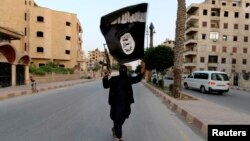 FILE - A member loyal to the Islamic State waves an IS flag in Raqqa, June 29, 2014. 