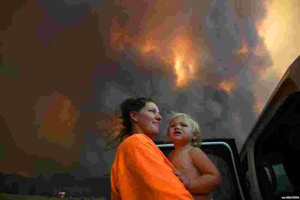 Sharnie Moren and her 18-month-old daughter Charlotte look on as thick smoke rises from bushfires near Nana Glen, near Coffs Harbour, Australia. (Credit: AAP Image/Dan Peled)