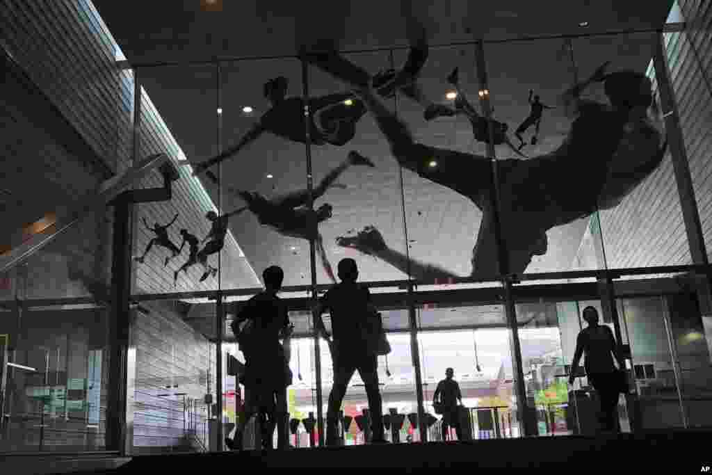 People look at the glass entrance of a subway station in Singapore, which is decorated with decals of athletes in action.