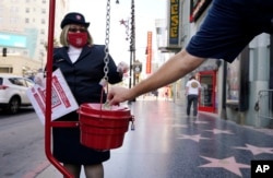 FILE - A pedestrian drops a dollar into a collection basket as Michelle Miranda of The Salvation Army looks on during the charitable organization's drive-through donations event at the TCL Chinese Theatre, Thursday, Dec. 10, 2020, in Los Angeles. (AP Photo/Chris Pizzello, File)