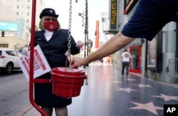 FILE - A pedestrian drops $1 into a donation basket as Michelle Miranda of the Salvation Army looks on during the charity's drive-thru donation event at the TCL Chinese Theater in Los Angeles on Thursday, Dec. 10, 2020.  (AP Photo/Chris Pizzello, File)