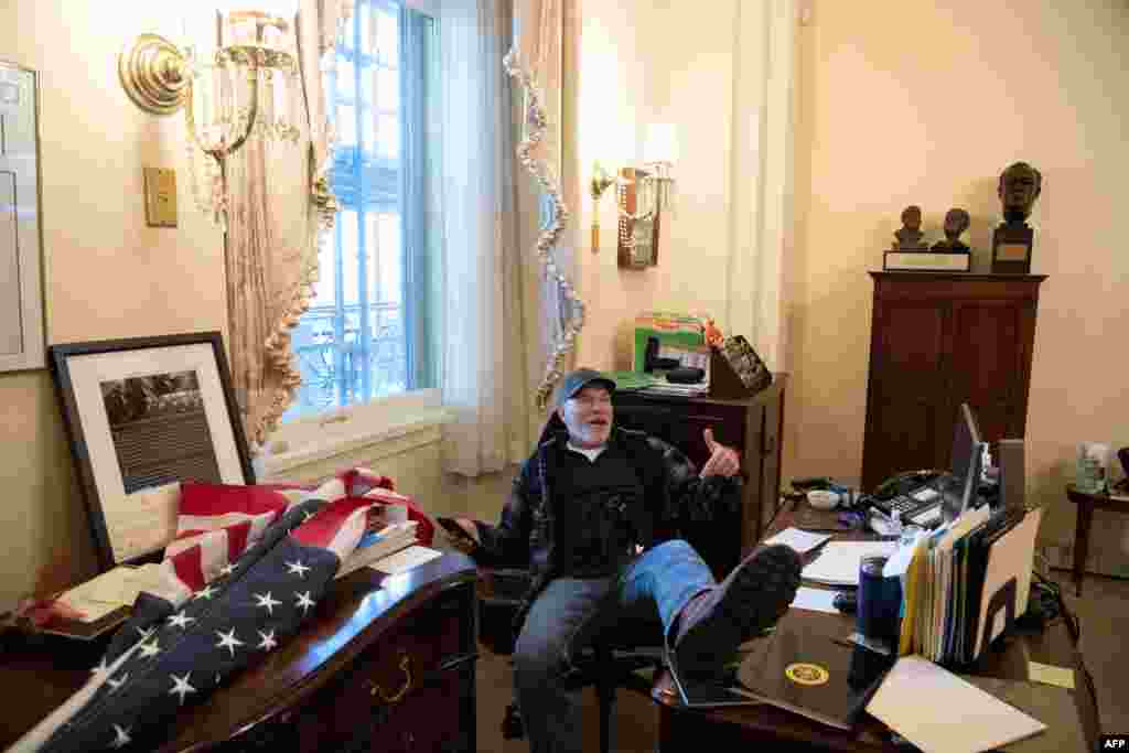 A supporter of President Donald Trump sits inside the office of Speaker of the House Nancy Pelosi inside the Capitol in Washington as demonstrators breeched security and entered the Capitol.