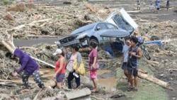 Orang-orang melewati kendaraan hancur dan puing kayu akibat hujan lebat Badai Tropis Trami di Laurel, Batangas, selatan Manila, 25 Oktober 2024. (Foto: AFP)