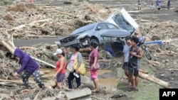 Orang-orang melewati kendaraan hancur dan puing kayu akibat hujan lebat Badai Tropis Trami di Laurel, Batangas, selatan Manila, 25 Oktober 2024. (Foto: AFP)