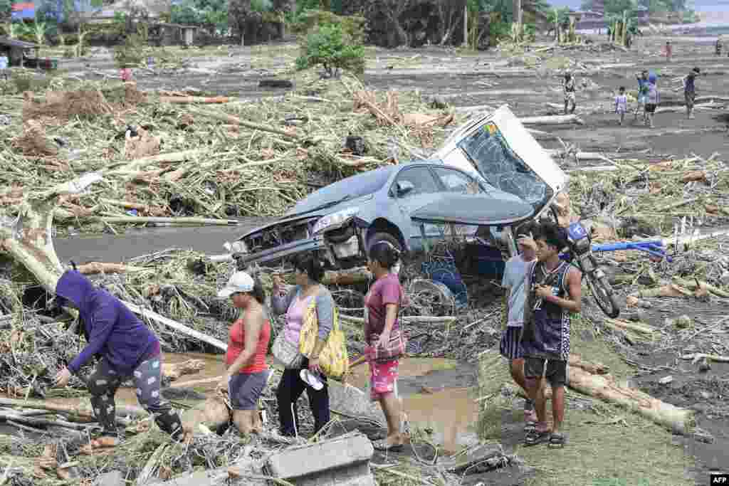 People walk past destroyed vehicles swept away along with debris of logs due to heavy rains brought about by Tropical Storm Trami in Laurel, Batangas province, south of Manila.