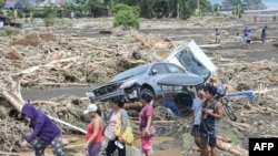 People walk past destroyed vehicles swept away along with debris of logs due to heavy rains brought about by Tropical Storm Trami in Laurel, Batangas province, south of Manila.
