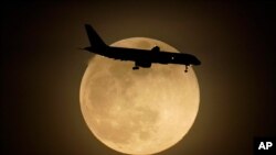FILE - In this April 26, 2021, photo, a jet is silhouetted by the rising moon as it approaches Louisville International Airport in Louisville, Ky.