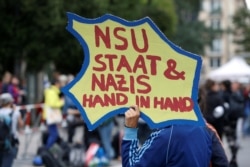 FILE - A protester holds a placard reading "NSU State &amp; Nazis Hand in Hand" in front of a Munich court during the trial of a suspected NSU member, in Munich, Germany, July 11, 2018.