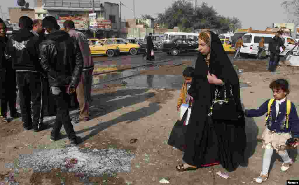 A woman and her children walk past the site of a suicide bombing in the Shi&#39;ite neighborhood of Kadhimiya in Baghdad, Feb. 9, 2015.