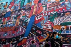 People wearing protective face masks to help curb the spread of the new coronavirus walk by a giant painting depicting the capital city at 798 art district in Beijing, Sunday, April 26, 2020.