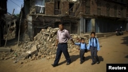 Birendra Karmacharya (kiri) berjalan melewati puing-puing rumah sambil menggandeng anaknya Saksham Karmacharya, 4, dan Biyon Karmacharya (kanan), 9, menuju sekolah di Bhaktapur, Nepal, 31 Mei 2015. 