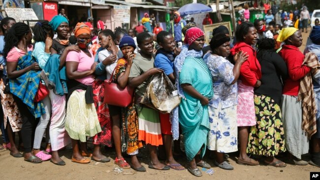 FILE - Women queue for a planned distribution of food for those suffering from the impact of the coronavirus pandemic, at a site in the Kibera slum of Nairobi, Kenya, April 10, 2020.