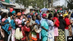 FILE - Women queue for a planned distribution of food for those suffering from the impact of the coronavirus pandemic, at a site in the Kibera slum of Nairobi, Kenya, April 10, 2020.