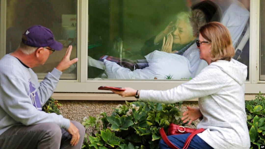 FILE - Judie Shape, center, blows a kiss to her son-in-law as her daughter looks on, as they visit on the phone and look at each other through a window at the Life Care Center in Kirkland, Wash., March 11, 2020.