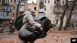 A woman carries her child as they evacuate from a residential building which was hit by a Russian rocket at the city center of Kharkiv, Ukraine, Jan. 30, 2023.