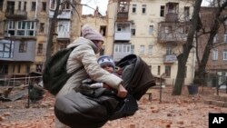 Una mujer carga a su hijo mientras evacuan un edificio residencial que fue alcanzado por un cohete ruso en el centro de la ciudad de Kharkiv, Ucrania, el lunes 30 de enero de 2023.