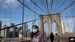 A woman wears a mask as she crosses the Brooklyn Bridge in New York, March 16, 2020. The bridge's pedestrian path is normally crowded on a sunny day.