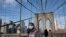 A woman wears a mask as she crosses the Brooklyn Bridge in New York, March 16, 2020. The bridge's pedestrian path is normally crowded on a sunny day.