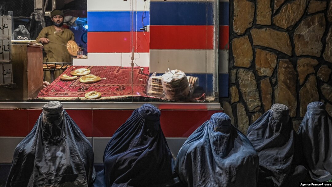 FILE - Afghan burqa-clad women sit in front of a bakery as they seek alms in Kabul, Jan. 6, 2022. 