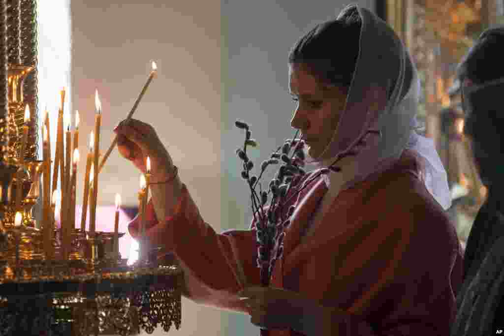 A woman lights a candle during the Palm Sunday Mass inside the St. Peter&#39;s Cathedral in the High-Petrovsky monastery in Moscow, Russia.