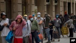 People line up as they wait to receive a ration of donated food by volunteers of the Santa Ana church in Barcelona, Spain, May 14, 2020. 