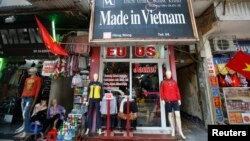 FILE - Vendors sit outside a shop selling clothes in Hanoi, Oct. 3, 2014.