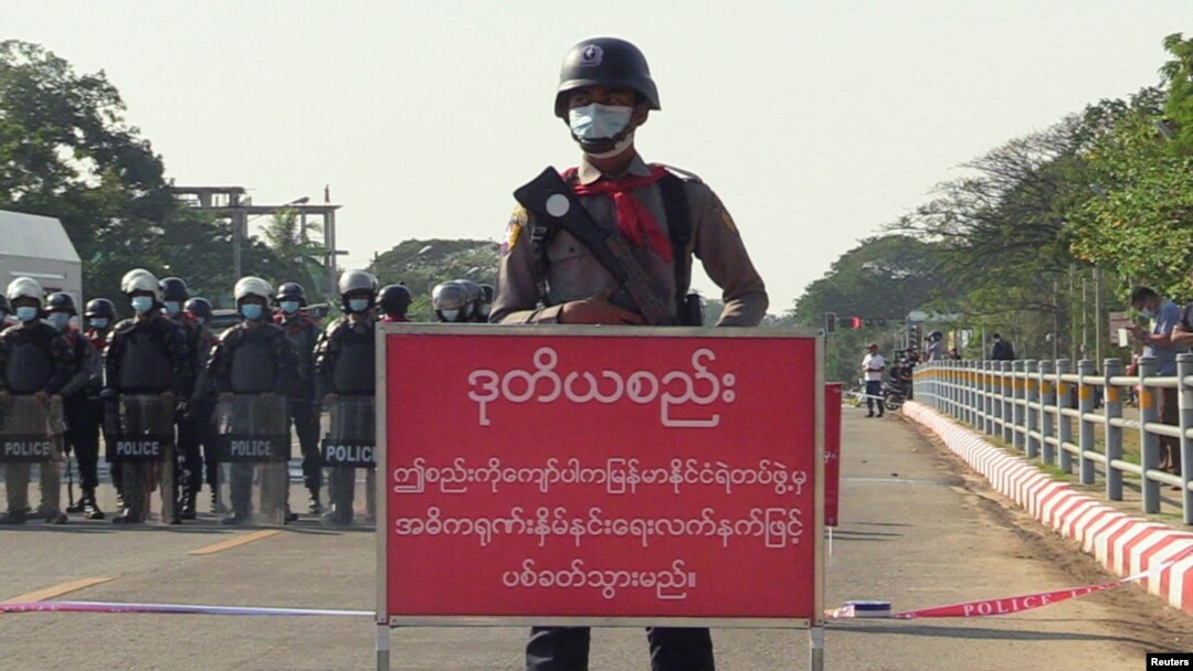 FILE - Policeman stands behind a banner reading "if this line is crossed, Myanmar police force will fire with live ammunition" during a protest against the military coup and to demand the release of Aung San Suu Kyi, in Naypyitaw, Myanmar, February 8, 2021.