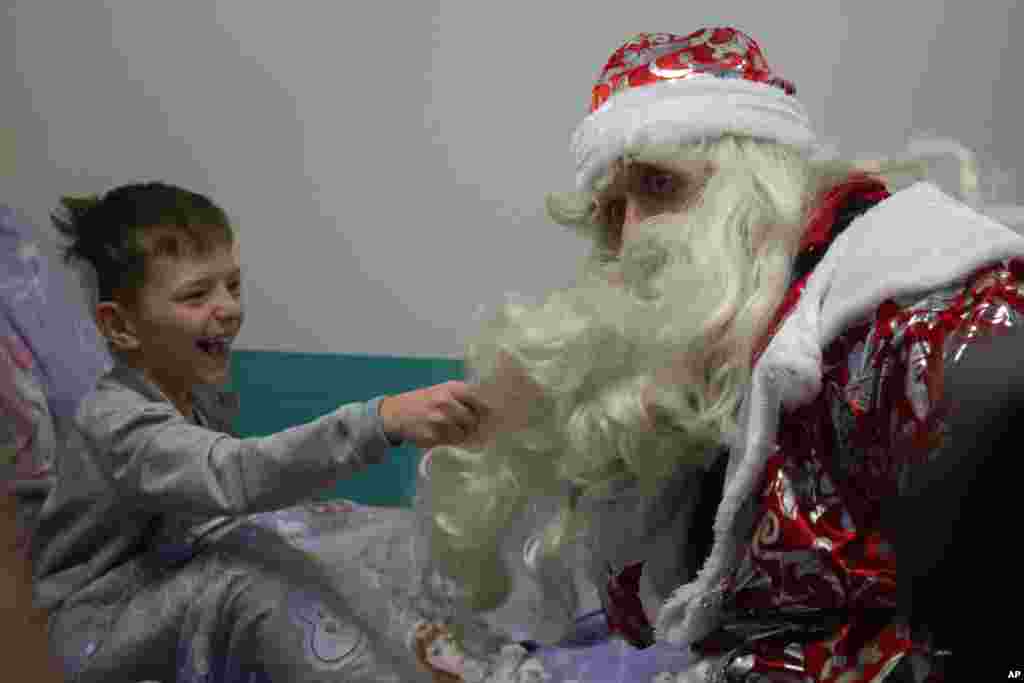 A boy pulls the beard of a Russian emergency rescue worker dressed as Ded Moroz (Santa Claus, or Father Frost ) after scaling the wall at a children hospital in Moscow.