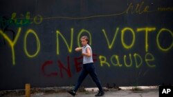 Una transeúnte pasa frente a un grafitti en Caracas que censura la elección presidencial del 20 de mayo, califcándola de fraude.