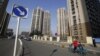 FILE - A woman rides a tricycle carrying a child near a residential compound in Beijing's Tongzhou district, China.