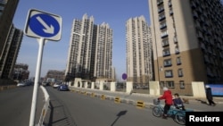 FILE - A woman rides a tricycle carrying a child near a residential compound in Beijing's Tongzhou district, China.