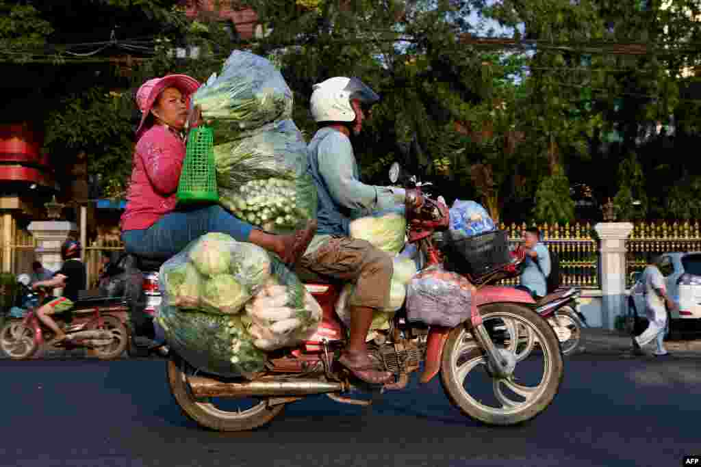 A woman holds piles of vegetables transported by motorcycle along a street in Phnom Penh, Cambodia.